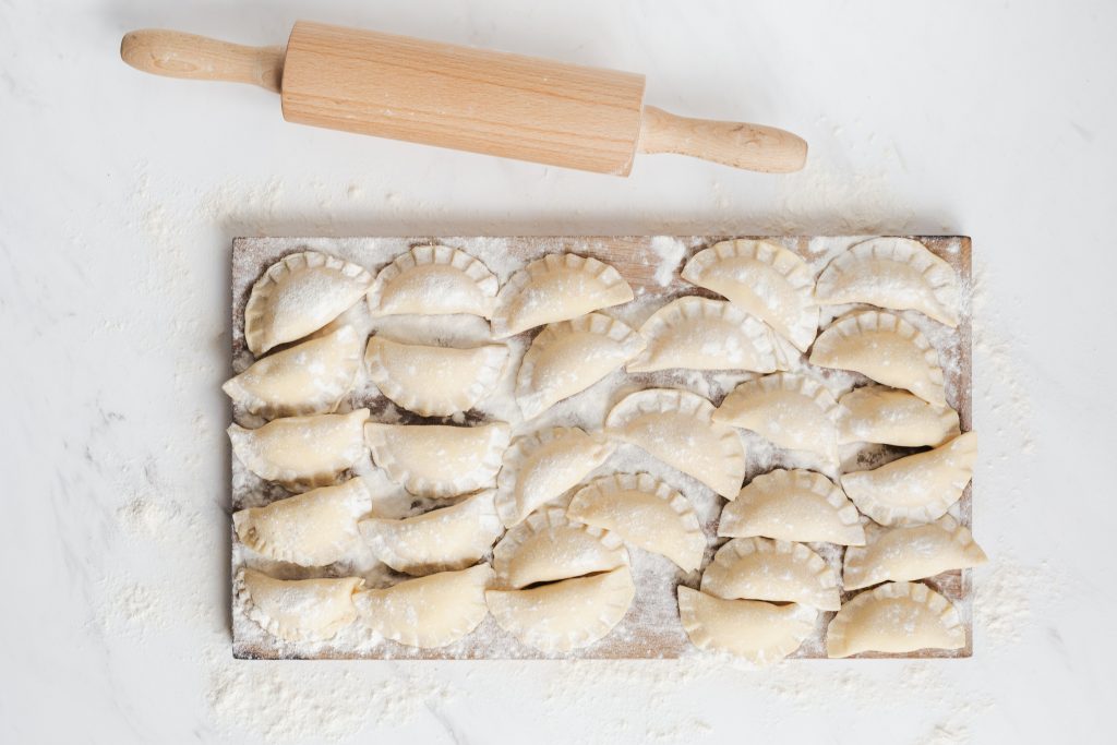 Raw Pierogi on a flour dusted chopping board with a rolling pin next to it